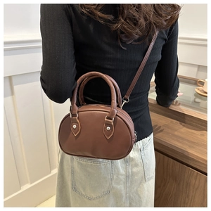 Dettaglio di una borsa in pelle marrone semi-ovale con rivetti argentati e manici eleganti