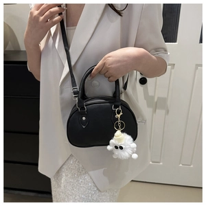 Detail of a black leather crescent crossbody bag with a white plush monster charm