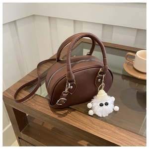 Dettaglio di una borsa ovale marrone con ciondolo in peluche su un tavolo di legno