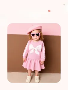 Détail d'une robe de fille rose à manches longues en coton avec un grand nœud blanc
