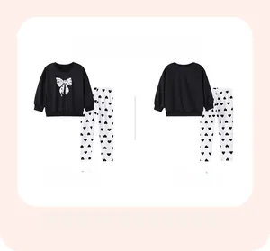 Flat lay of girl's black sweatshirt with bow print and heart pattern leggings set