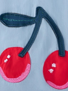 Detail of red cherry embroidery applique on light blue denim sleeveless girl's dress