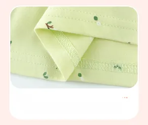 Détail de l'ourlet de robe bébé avec coutures fines et imprimé feuilles sur tissu vert
