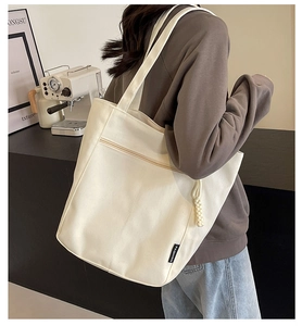 Detail of off-white canvas tote bag featuring front zipper pocket and fashion label