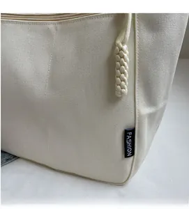Detailed macro view of the cream canvas tote bag with zipper closure and woven charm