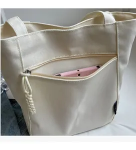 Close-up of front zipper pocket on beige canvas tote bag showing storage capacity