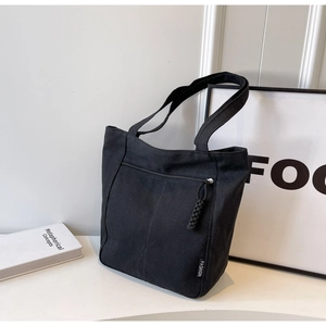 Detail of black canvas tote bag showing front zipper pocket and Fashion label branding