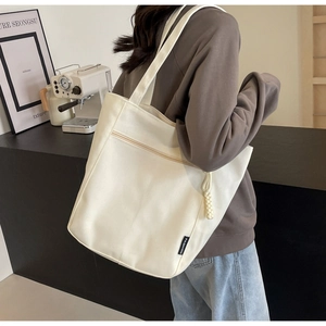Detail of white canvas tote bag with fashion label and woven charm on model's shoulder