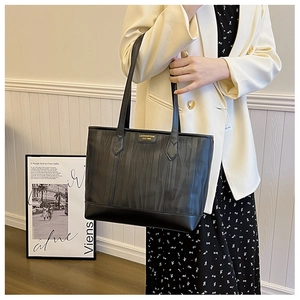 Detail of black tote bag with vertical wavy texture and gold metal logo plaque