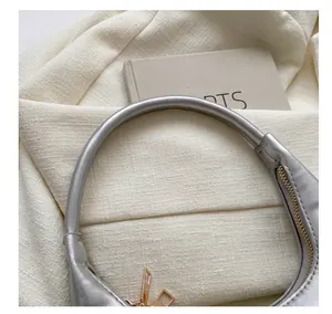Detail of silver faux leather handbag featuring a curved handle and golden zipper