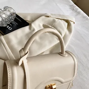 Macro shot of minimalist cream leather handbag with knotted handle and gold hardware