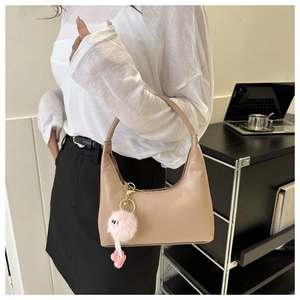 Chic beige crescent underarm bag shown with a playful pink plush monster charm on a shoulder