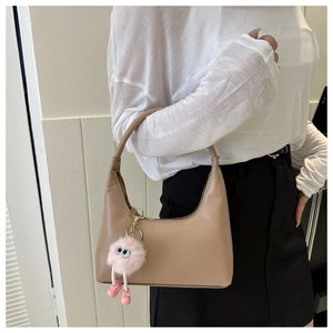 Chic beige hobo bag with a cute pink monster pom-pom charm shown in a lifestyle scene