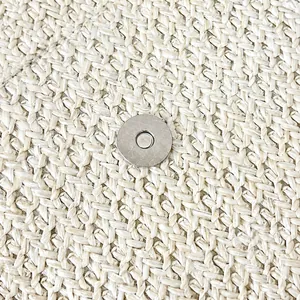 Gros plan du fermoir magnétique argenté sur la texture du sac à bandoulière en paille