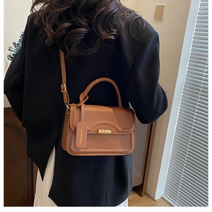Caramel brown handbag over the shoulder of a model in a black blazer and white dress