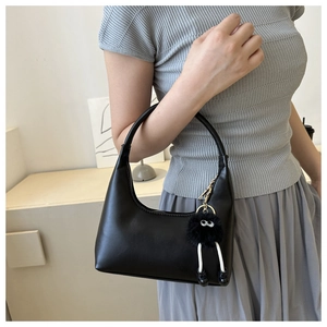 Chic black half-moon hobo bag with unique fluffy monster charm detail on a model