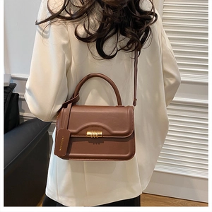 Brown leather handbag detail featuring gold cylindrical lock and a fashion tag charm