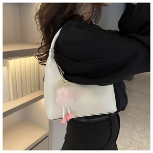 Elegante borsa hobo beige con pompon di pelliccia rosa portata a spalla per un look chic