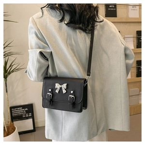 Detail of black crossbody bag with silver bow accent and twin straps shown on model