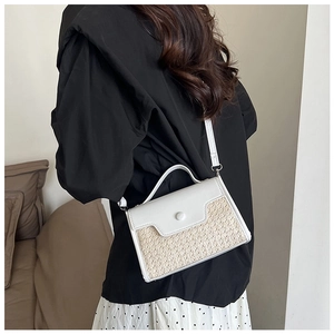Détail d'un sac à bandoulière en paille tressée et cuir blanc porté par un mannequin chic