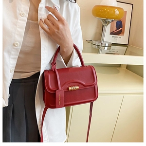 Detail of wine red crossbody bag with golden twist lock and fashion tag on model
