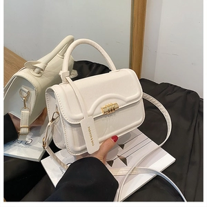 Detail view of cream white shoulder bag featuring gold cylinder lock and fashion tag