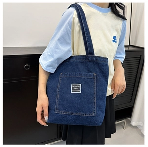 Détail du sac cabas en jean bleu avec bandoulière renforcée et poche carrée à l'avant