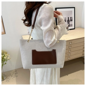 Detail einer beigen Canvas-Tasche mit brauner Ledertasche und goldener Kette