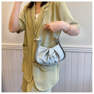 Sac croissant argenté plissé avec boucle papillon et poignée perlée sur un tailleur vert