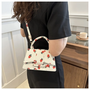 Detail van witte handtas met aardbeienprint en gebogen handvat aan de schouder