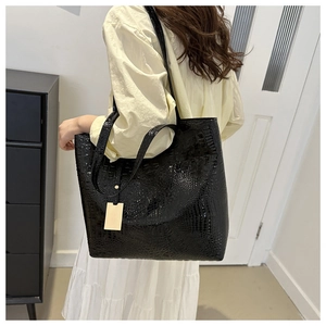 Detail shot of black crocodile pattern tote bag with gold metal tag on shoulder strap