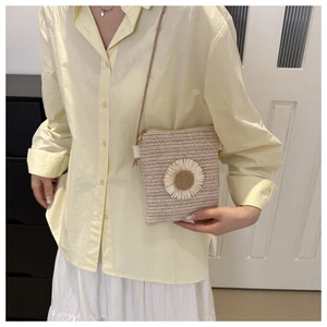 Dettaglio di una borsa a tracolla intrecciata a fiori in paglia beige con cerniera