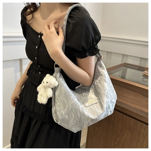 Bolso hobo plateado con textura plisada y colgante de oso blanco en una modelo