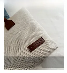 Close-up of beige textured canvas bag with a brown leather patch and Fashion logo