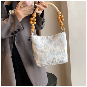 Détail d'un sac à main brodé de papillons avec poignée en bois porté par un mannequin