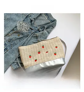 Detail of straw woven bucket bag with red strawberry embroidery and silver strap