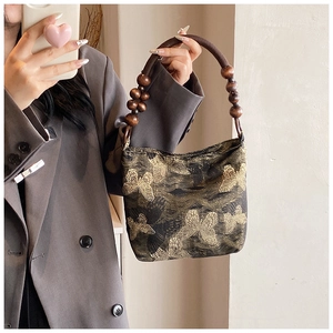 Dettaglio del ricamo a farfalla dorata e manico in perle di legno vintage della borsa