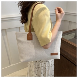 Detail of canvas tote bag with brown faux leather strap and small fashion logo tag