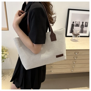 Detailed shot of large cream canvas and brown leather tote bag worn by a model