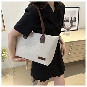 Detail of cream canvas tote bag featuring brown leather straps and fashion label tag
