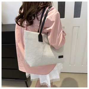 Detail of minimalist canvas tote bag with black leather straps and brand label on ivory fabric