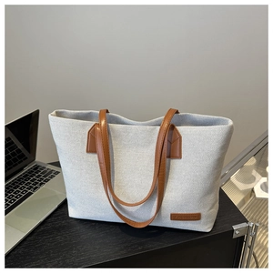 Detail of grey knitted canvas tote bag featuring brown leather handles and brand tag