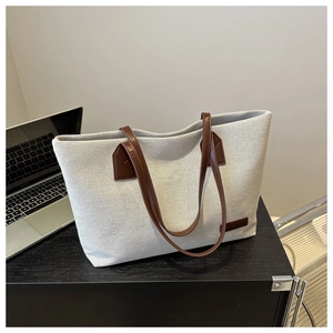 Close-up of beige canvas tote bag featuring brown leather handles and brand logo tag
