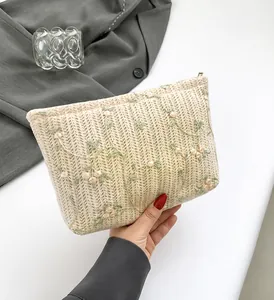 Detail of hand-held beige knitted clutch bag with floral embroidery and metal zipper