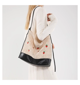Detail of woven straw bucket bag with red strawberry embroidery and black leather base