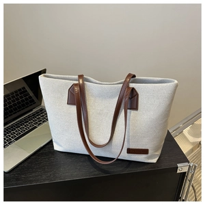 Close-up of beige canvas tote bag with brown leather handles and a fashion leather label
