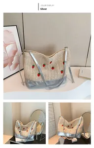 Detail view of woven straw bucket bag with red strawberry embroidery and silver straps