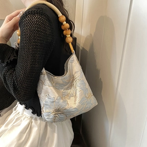 Blaue Jacquard-Schultertasche mit Perlenriemen an der Schulter des Models