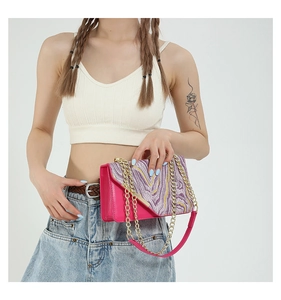 Detail of fuchsia patent leather bag featuring purple and yellow embroidery with gold chain