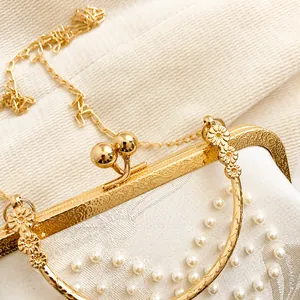 Détail du fermoir fleuri doré et des perles blanches sur le sac de soirée vintage